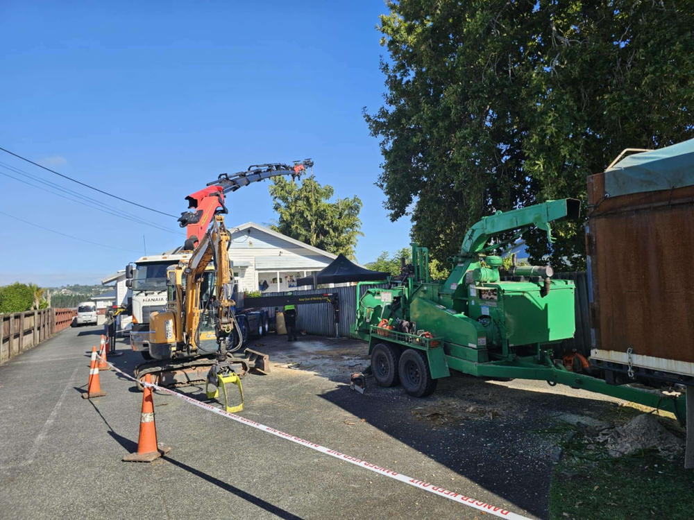 Roadside job with a crane truck, excavator and wood chipper working inside a coned-off safety zone
